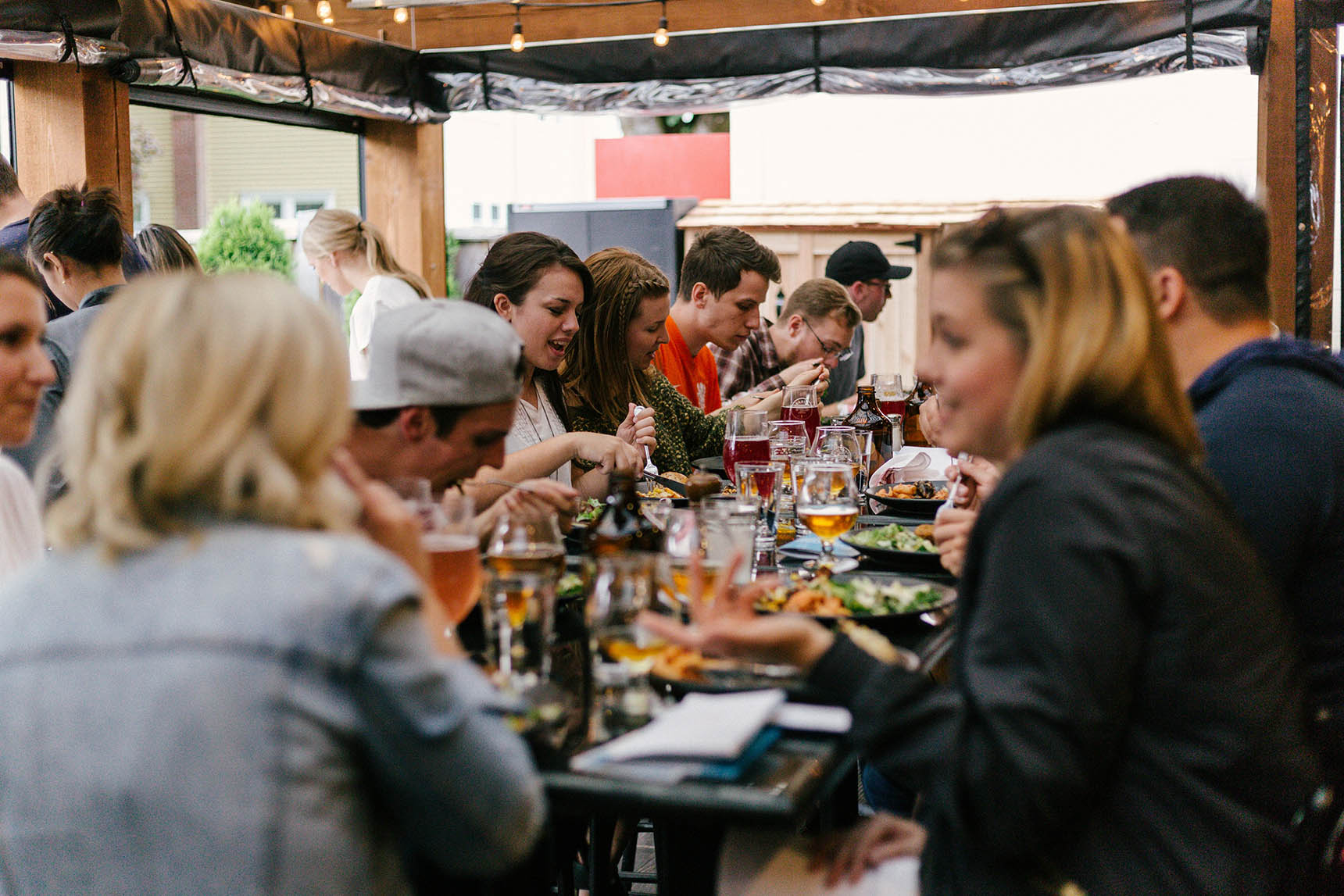 Young People Are Sitting Around The Table Drinking Beer, Eating And Chatting