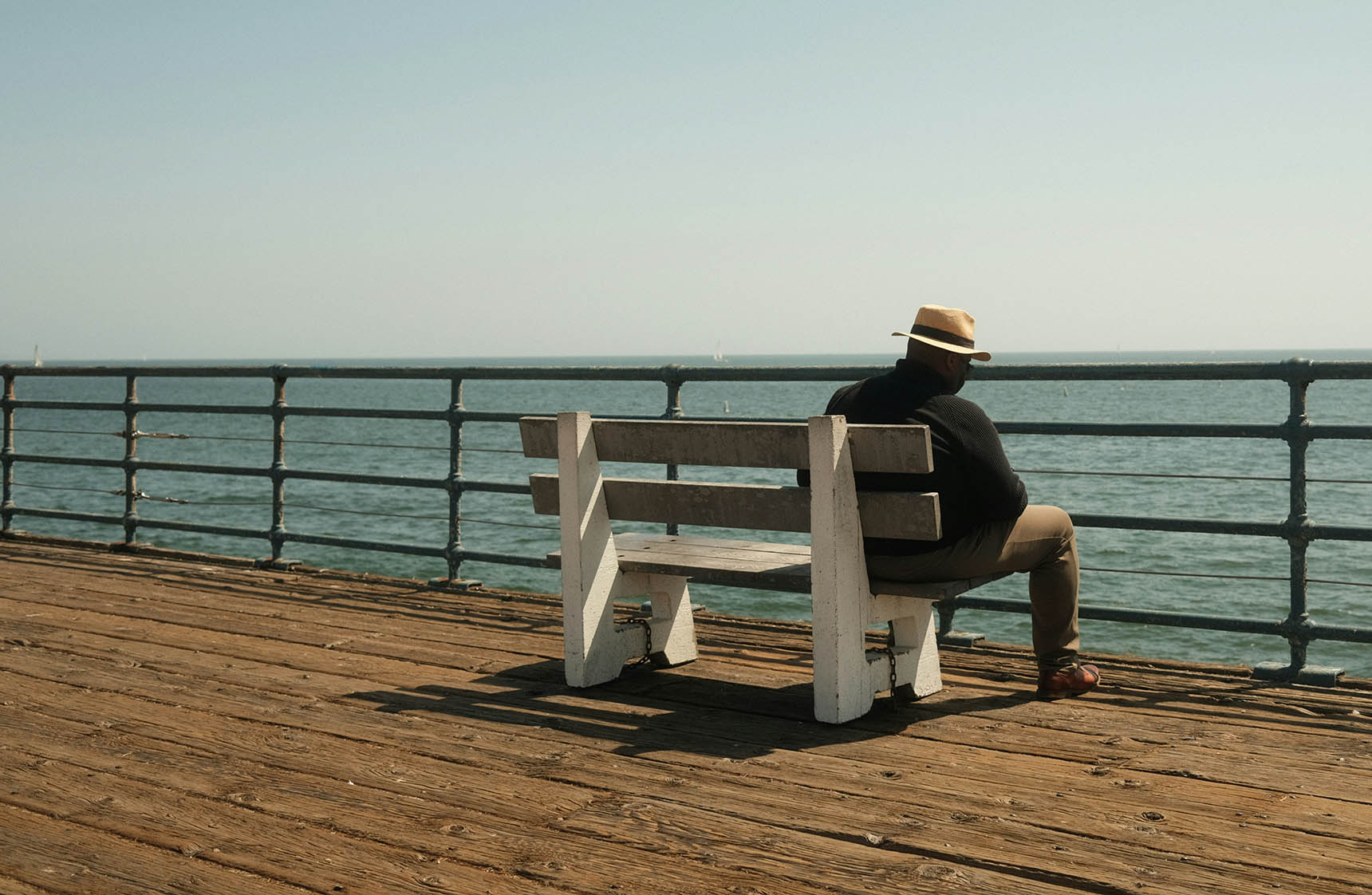 A Man Wearing A Hat Is Sitting Alone On The Bench Near The Sea Feeling Social Isolation