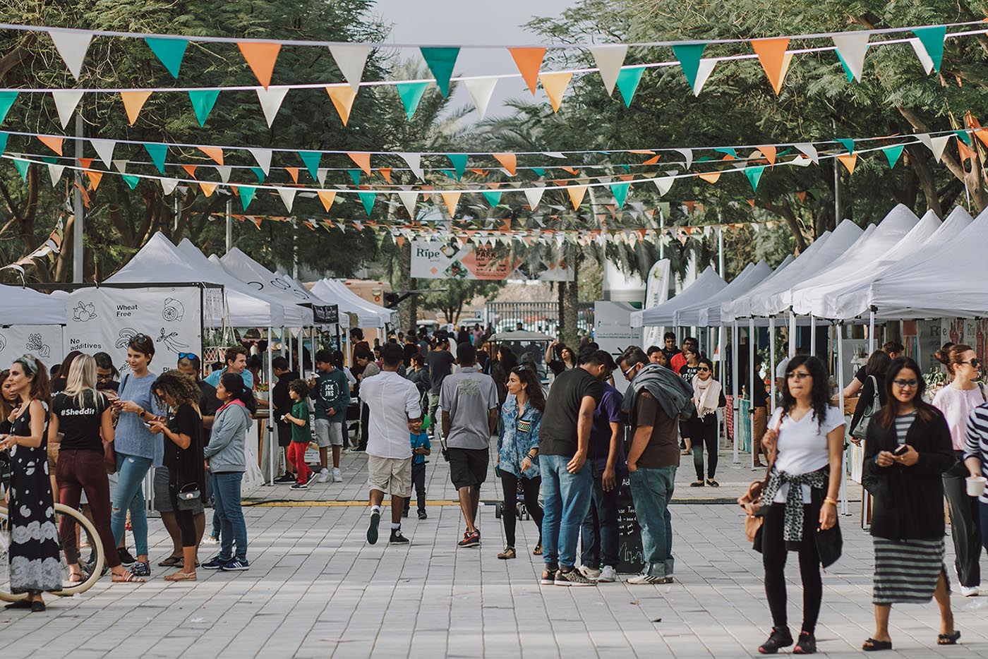 People Are Walking Around The Weekend Market Along A Tree-Lined Alley